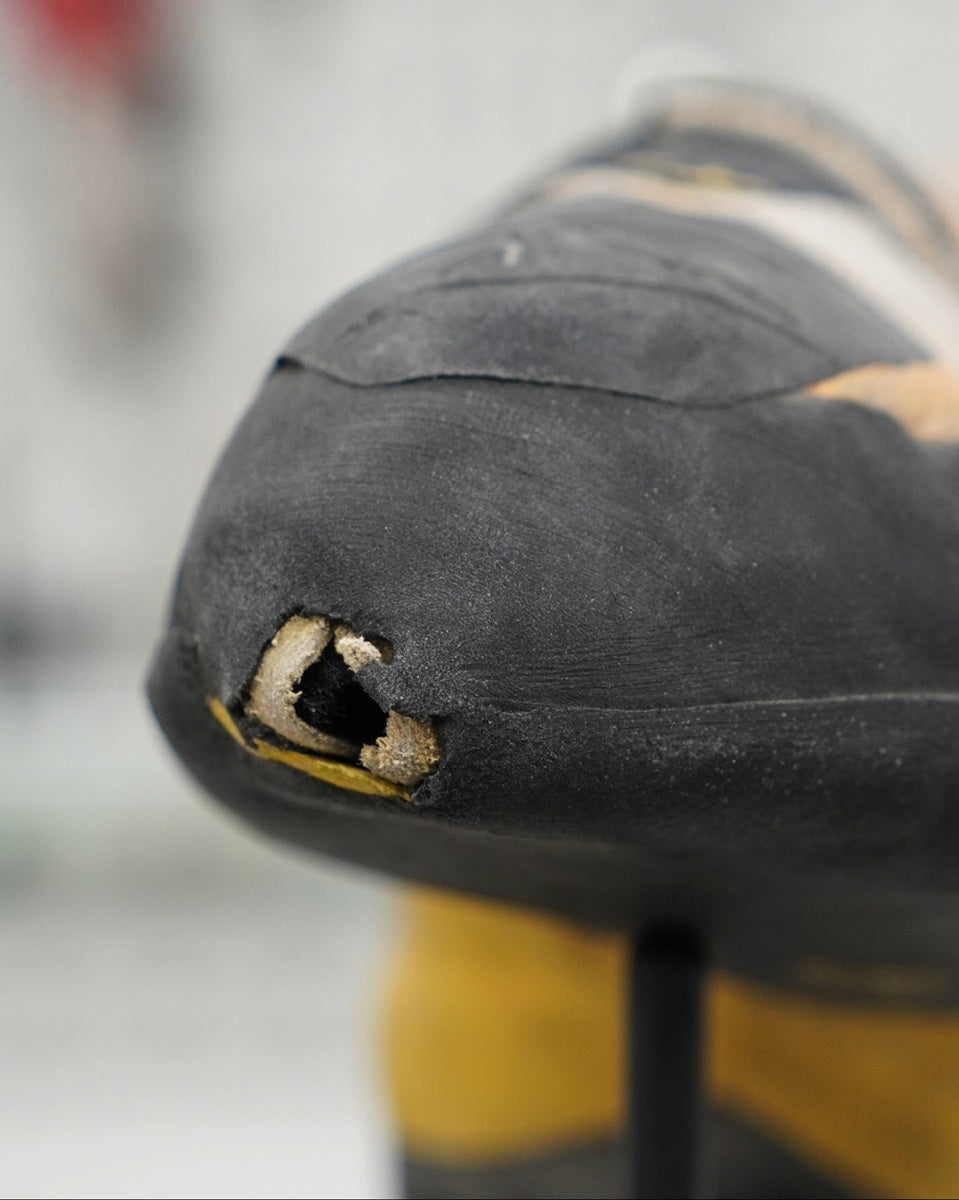 Close-up of a worn-out black and yellow shoe sole with a hole.