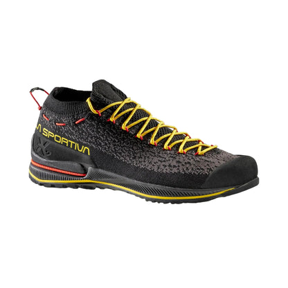Black athletic shoe with yellow laces on a gray background