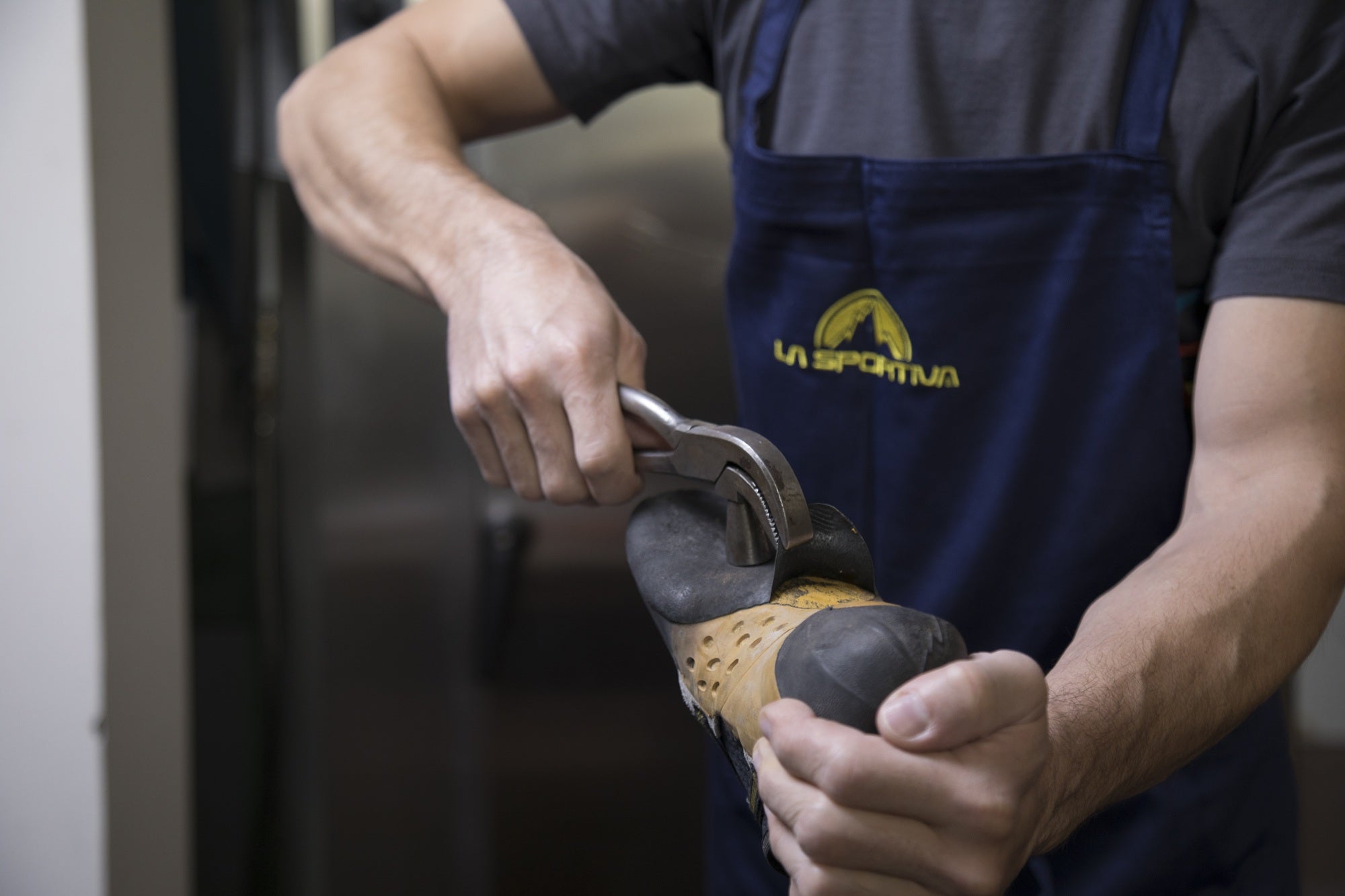 Person using a tool on a shoe, wearing a blue apron with a logo.